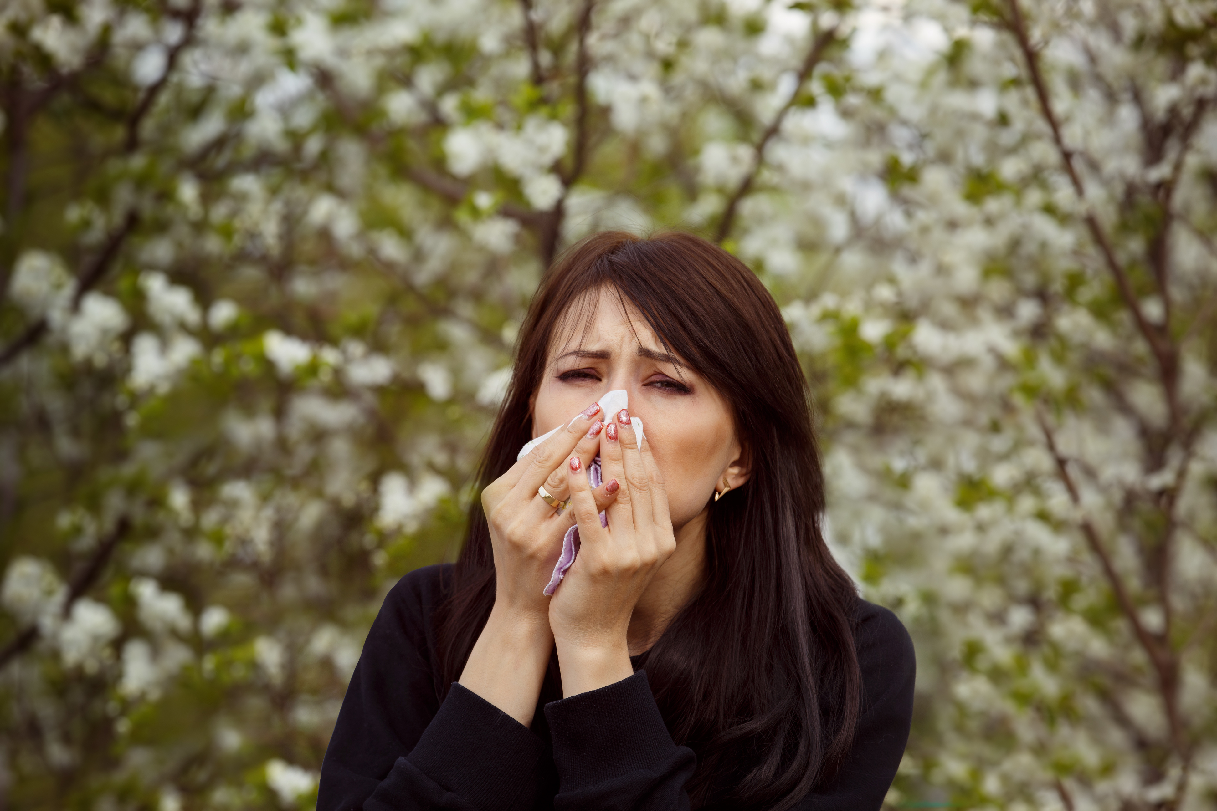 Portrait of sick sneezing woman at spring outdoors blossoms background.