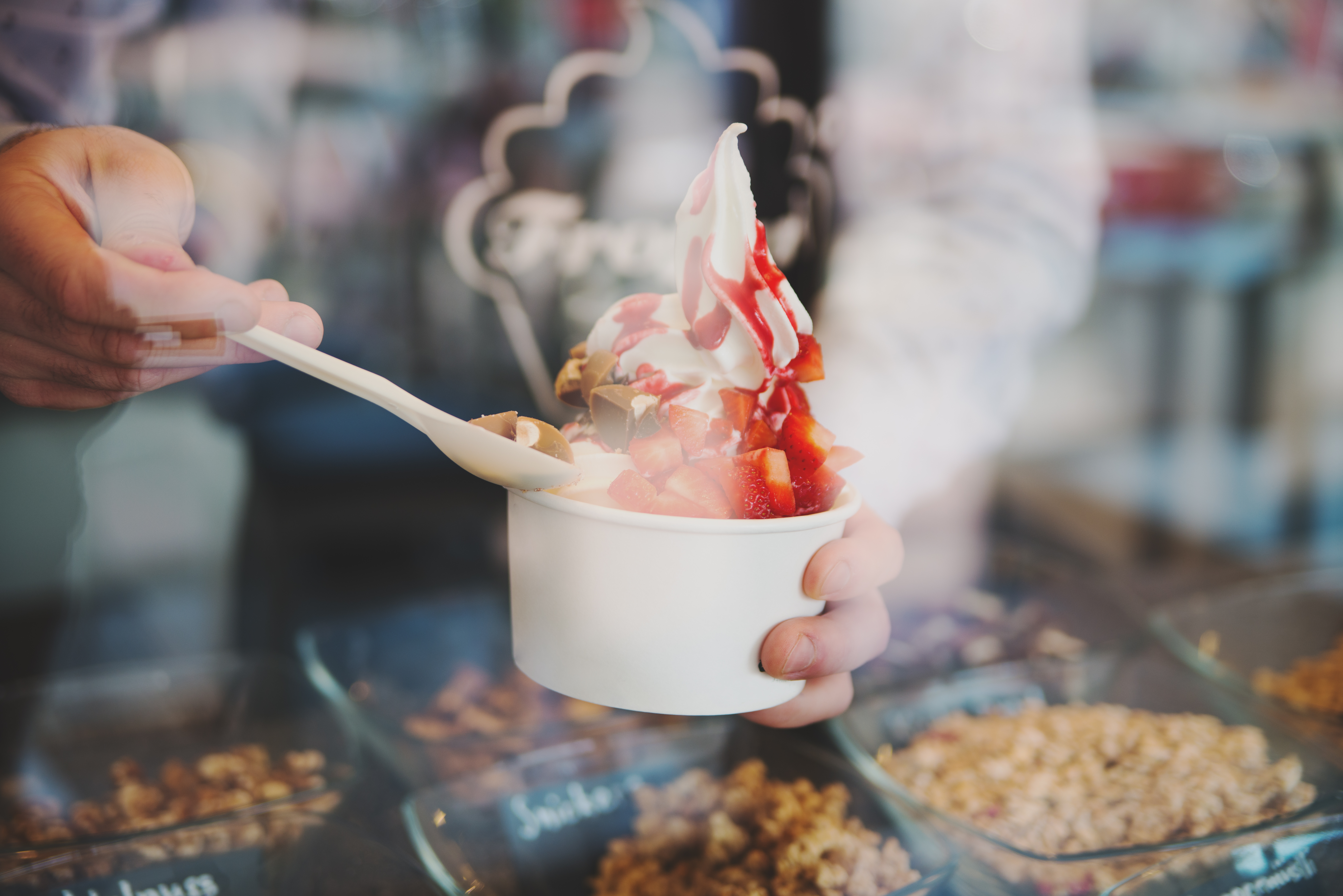 seller pours sauce on a soft frozen yogurt in white take away cup